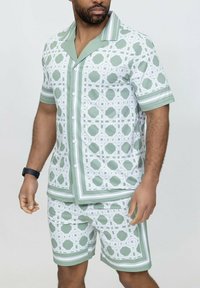 Ensemble composé d'une chemise à manches courtes et d'un short en vert clair avec un motif géométrique blanc, présentant des accents de col et d'ourlet contrastants, fabriqué en tissu léger.