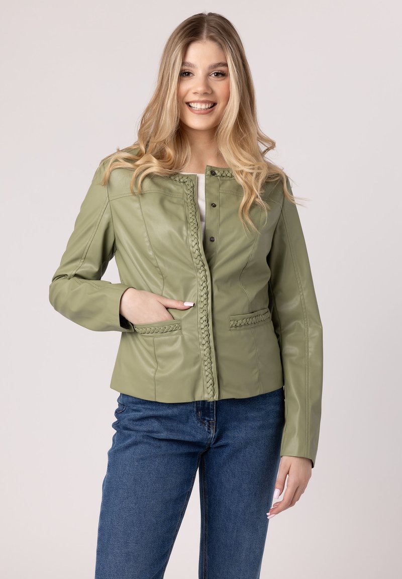 Groene leren jasje met een gevlochten voorzijde, drukknopen en twee voorzakken, gecombineerd met blauwe spijkerbroek op een neutrale achtergrond.
