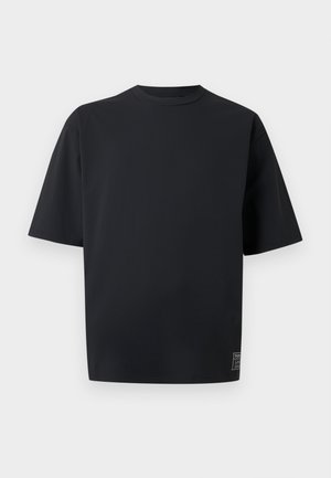 T-shirt noir surdimensionné à manches courtes avec col rond et petite étiquette de marque près de l'ourlet inférieur sur un fond clair uni.