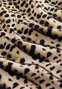 Tissu beige avec des taches noires irrégulières imprimé léopard, présenté avec des plis doux et des rides.
