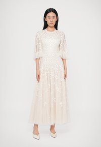 Dlhé, priehľadné, krémovo biele šaty s vyšívanými kvetinovými detailmi, krátkymi nadýchanými rukávmi a prúdiacou sukňou. Ukončené okrúhlym výstrihom.