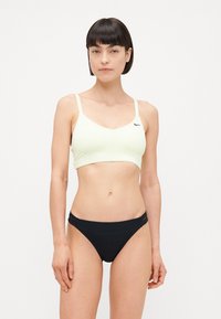 Soutien-gorge de sport jaune clair avec des bretelles fines et un logo Nike noir, assorti à un bas de bikini noir avec des accents de double sangle.