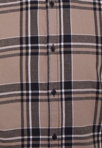 Tkanina w kratkę w odcieniach beżu i czerni z czterema czarnymi guzikami w pionowej linii na środku.