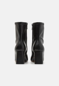 Bottines noires en cuir avec un talon carré, présentant une texture lisse et des zips sur les côtés, affichant une silhouette ajustée.