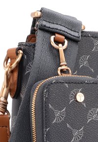 Borsa in tessuto nero con texture, dotata di hardware dorato, tasca con cerniera, dettagli in pelle marrone e un sottile motivo floreale.