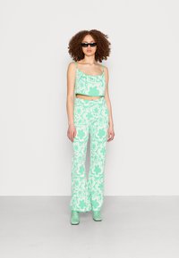 Conjunto de duas peças verde menta, featuring uma blusa cropped com padrões florais e calças largas. Inclui botas de salto verdes combinando e óculos de sol.