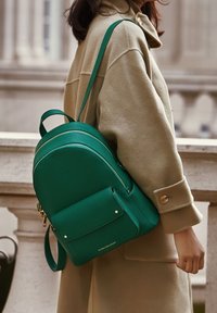 Grön läderryggsäck med rundad form, dubbla dragkedjor, framficka och guldaccenter. Texturerad yta med justerbara remmar.