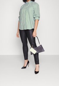 Grøn- og hvidstribet button-up skjorte, sorte skinny bukser, sorte patenterede højhælede sko og en lille sort håndtaske med en lys grøn detalje.