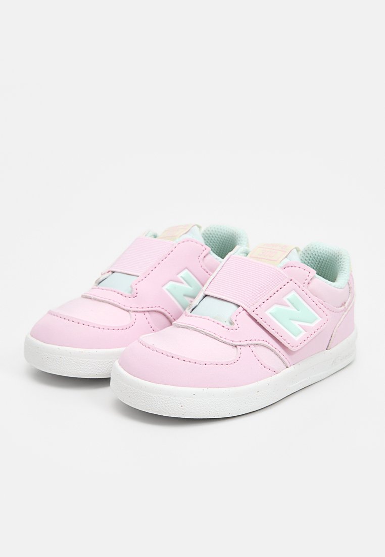 Baskets pour tout-petits roses avec des bandes velcro, affichant un logo 'N' en accent menthe, en matière synthétique lisse et semelles en caoutchouc blanches.