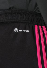 Svarta träningsshorts med ett rosa rand, elastisk midja och en vit "AEROREADY"-logotyp på sidan. Slät textur.