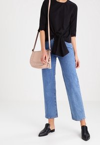 Svart, åtsittande topp med knutdetalj, ljusblå raka jeans, svarta klackskor och en rosa axelväska med vävda detaljer och en tofs.