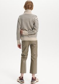 Suéter a rayas beige y azul marino con cuello alto, combinado con pantalones ajustados de imitación cuero verde oliva y zapatillas gruesas.