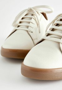 Sneaker bianchi in pelle con lacci piatti, punte arrotondate e suole in gomma. Superficie texture con dettagli di cucitura discreti.