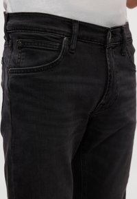 Mustad denim teksad sirge lõikega, viie taskuga disain, kerge pleekimine ja nähtav õmblus soonte ja taskute ääres.