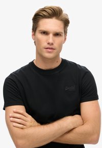 Sort t-shirt med kort ærme, rund halsudskæring og subtil logo-detalje på brystet, tætsiddende design og glat bomuldsstruktur.