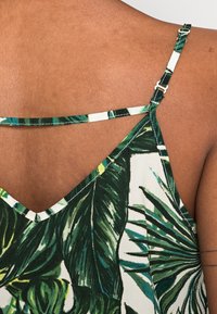 Camisole verde e bianca con motivo floreale, dotata di spalline regolabili, design a V e un tessuto morbido e testurizzato. Dettaglio significativo con doppia spallina sul retro.