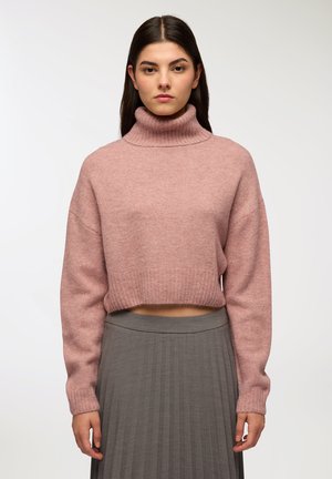 Maglione a collo alto cropped di un delicato rosa, realizzato in un morbido tessuto testurizzato, con colletto e polsini a coste, abbinato a una gonna grigia plissettata.