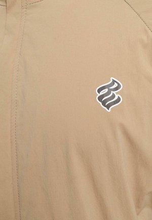 Šviesiai bežinė medžiaga pasižymi lygiu paviršiumi, subtiliu blizgesiu ir stilizuotu juodu logotipu dešinėje pusėje, kuriam būdingas kontrastingas baltas apvadas.