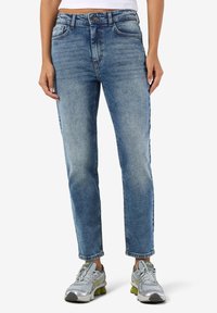 Lyseblå denimjeans med rette ben, fem lommer og synlig knapp- og glidelåslukking, brukt med grå joggesko.