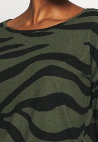 Grün-schwarz gestreifter Pullover mit Rundhalsausschnitt und weicher Stricktextur, mit einer lässigen Passform. Akzente setzen kräftige, wellenförmige Muster.