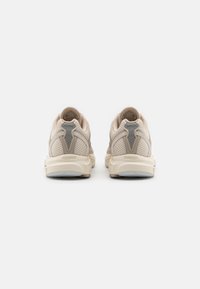 Beige mesh sneakers with a textured upper, soft padding, and contrasting light gray accents at the heel. Lightweight rubber sole.