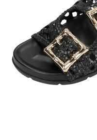 Sandalo intrecciato nero con suola spessa, caratterizzato da grandi fibbie quadrate metalliche dorate e una parte superiore testurizzata.