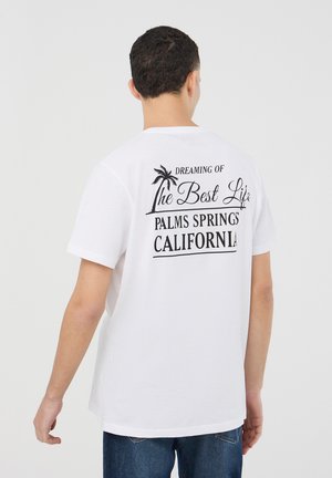 T-shirt bianco in cotone con stampa grafica nera sul retro, che presenta testo e un design di palma, maniche corte e vestibilità rilassata.