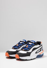 Baskets de sport noires, blanches et bleues en matériaux mesh et synthétiques ; avec des accents orange, des lacets ronds et une semelle épaisse.