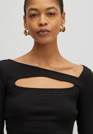 Schwarzes, geripptes Oberteil mit einem einzigartigen asymmetrischen Ausschnitt-Design, das lange Ärmel und eine weiche Textur aufweist. Goldene Creolen runden den Look ab.