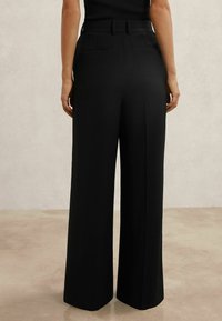 Čierne nohavice s širokými nohavicami vyrobené z hladkej látky. Majú priliehavý pás, pútka na opasok a dve zadné vrecká. Jednoduchý dizajn bez vzorov.