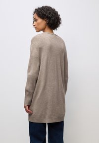 Beige dlouhý svetr s žebrovanými manžetami a lemem, vyrobený z měkké pleteniny, s uvolněným střihem a minimalistickým designem.