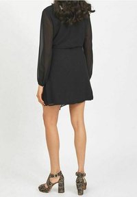 Robe noire avec de longues manches transparentes et une taille cintrée, associée à des escarpins rayés noir et beige avec une bride de cheville.