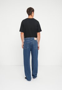 Svart t-skjorte med korte ermer, kombinert med løstsittende blå denimjeans med høy livhøyde, rett ben og synlige baklommer.
