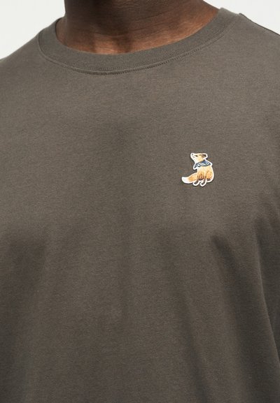 Καφέ κοντομάνικη μπλούζα με στρογγυλή λαιμόκοψη και μικρή κεντημένη αλεπού που φοράει μπλε κασκόλ στην αριστερή πλευρά του στήθους.