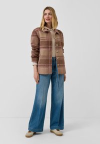 Brązowo-beżowa kraciasta kurtka z polaru z kołnierzem, guzikiem z przodu i luźnym krojem, w połączeniu z szerokimi niebieskimi dżinsami.
