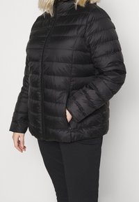Giacca piumino nera con cuciture orizzontali, colletto alto e zip frontale. Dotata di tasche laterali e texture liscia e lucida.