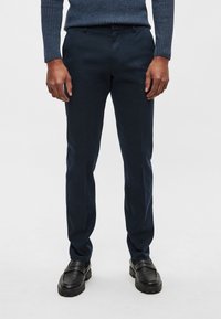 Marinblå chinos i skräddarsydd passform, gjorda av bomull. Har sidofickor, bältesöglor och en slät textur. Kombinerade med svarta skor.