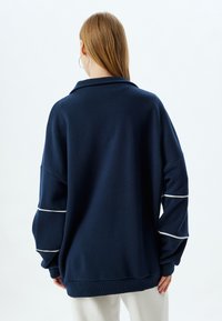 Sudadera de gran tamaño en azul marino con un alto cuello, rayas de acento blancas en las mangas y puños y dobladillo de canalé, hecha de una tela suave.