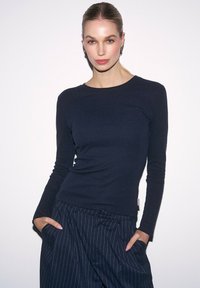 Granatowa bluzka z długim rękawem o prążkowanej fakturze, okrągły dekolt, dopasowany krój i lekka tkanina, zestawiona z spodniami w paski.
