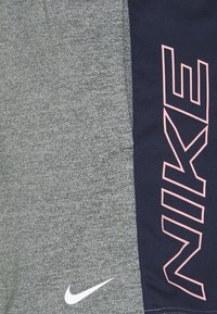 Shorts de sport gris avec un panneau latéral bleu marine. Présente un logo Nike blanc et le grand texte rose "NIKE" sur le bleu marine. Tissu texturé.