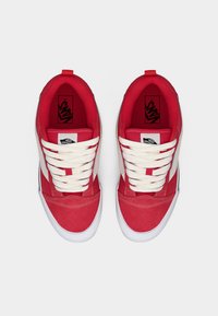 Κόκκινα πάνινα αθλητικά παπούτσια με λευκά κορδόνια, λευκές πλαϊνές ρίγες και λογότυπο στη γλώσσα. Διαθέτουν επενδυμένο κολάρο και λαστιχένια σόλα.