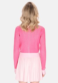 Rosa gerippter Pullover und ein hellrosa plissierter Rock. Der Pullover hat eine figurbetonte Silhouette mit langen Ärmeln und einem gerippten Saum.