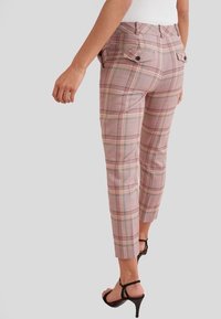 Pantalon à carreaux ajusté, longueur cheville, en rose, crème et vert, avec poches arrière et détails subtils de boutons. Finition en tissu texturé.