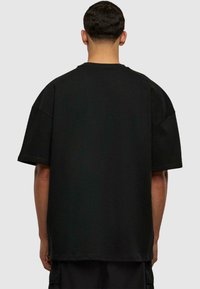 Fekete, oversized póló rövid ujjakkal és egyenes végződéssel. Puha pamutból készült, egyszerű, sima textúrával, minta nélkül.