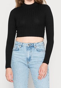 Black cropped ribbed sweater with long sleeves, high neckline, worn over light blue high-waisted jeans. Flat texture with subtle pattern.