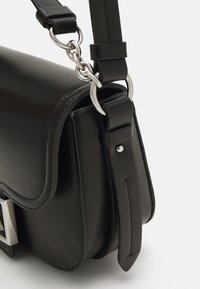 Borsa a spalla in pelle nera con chiusura a soffietto, hardware in argento, tracolla rimovibile e dettagli di cucitura visibili sulla superficie.
