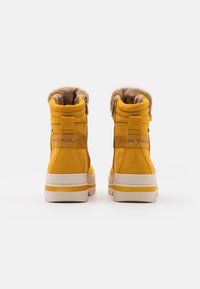 Bottes basses en daim jaune avec une doublure en fourrure douce, un col rembourré et une fermeture éclair ; elles comportent une semelle en caoutchouc rayée blanche et jaune.