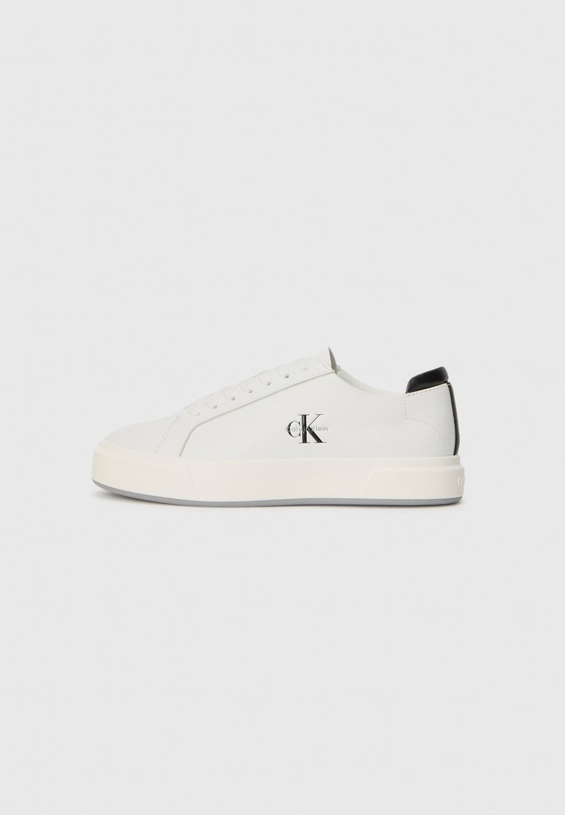 Adidași din piele albă cu vârf rotunjit, talpă plată din cauciuc și accent negru la toc. Prezintă un logo Calvin Klein negru proeminent pe lateral.