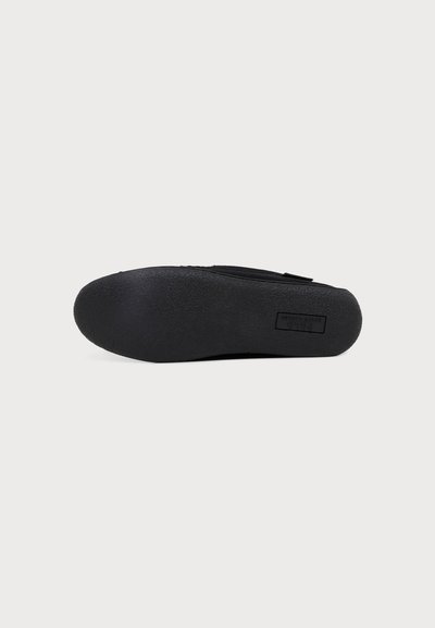 Semelle de chaussure noire plate avec surface texturée et zone rectangulaire pour logo, présentée sur un fond clair uni.