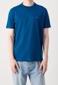 Modré bavlněné tričko s kulatým výstřihem, krátkými rukávy a jemným logem "BOSS" vpředu. Nosené s světle modrými džíny.